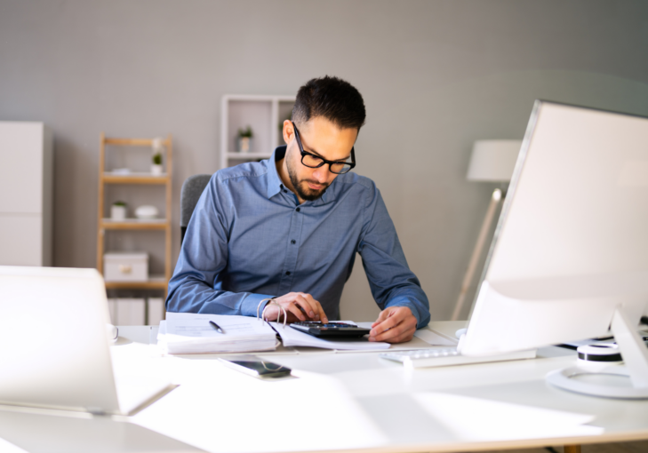 man sitting at desk typing on a calculator